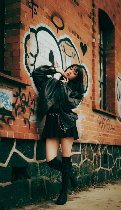 Free Stylish woman poses against graffiti-covered brick wall, showcasing urban street fashion. Stock Photo