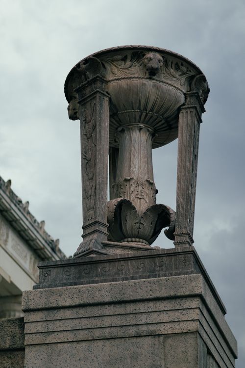 Free A classical stone urn sculpture with intricate carvings, set against a dramatic cloudy sky. Stock Photo