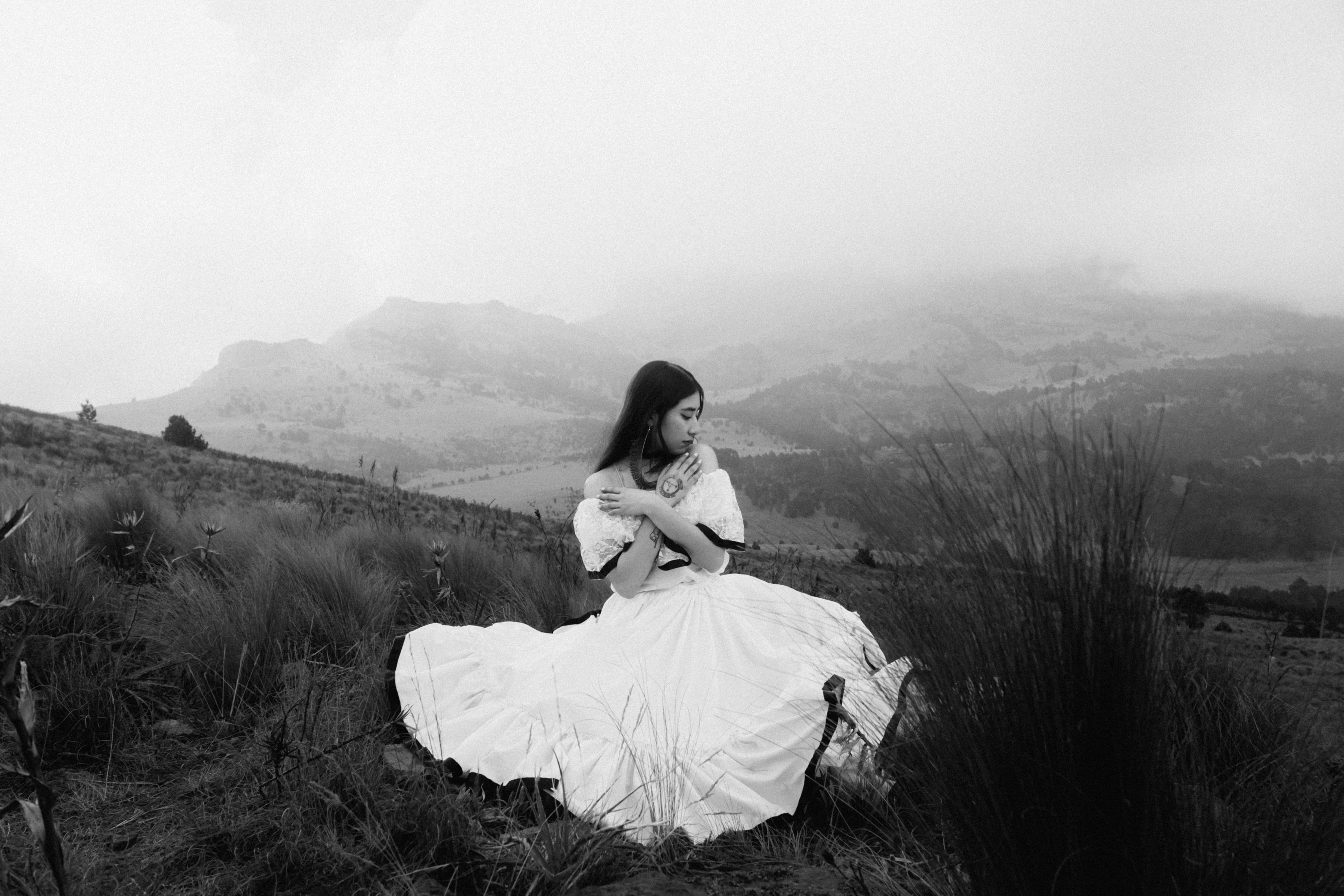 A woman in a white dress sits in a foggy mountain landscape, creating a serene and ethereal scene.