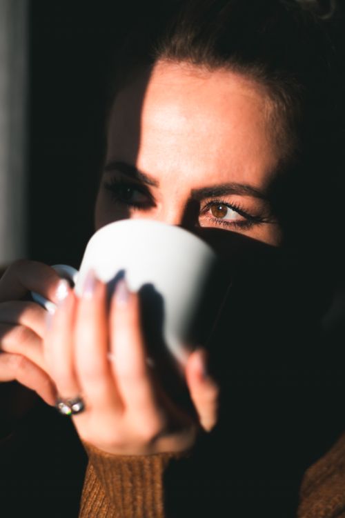 Free Woman enjoying a warm cup of coffee, captured in an intimate close-up with natural lighting. Stock Photo