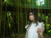 Portrait of a young woman in white dress surrounded by hanging vines in a lush forest setting.