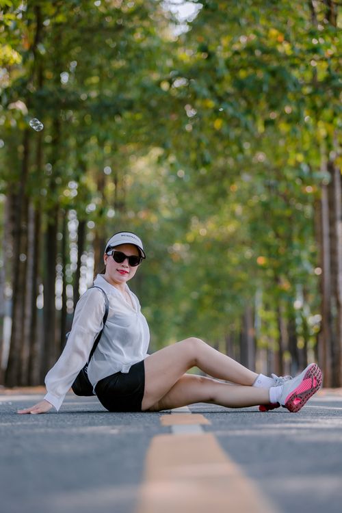 Free Stylish woman sitting on a forest path, wearing sunglasses and a casual outfit. Stock Photo