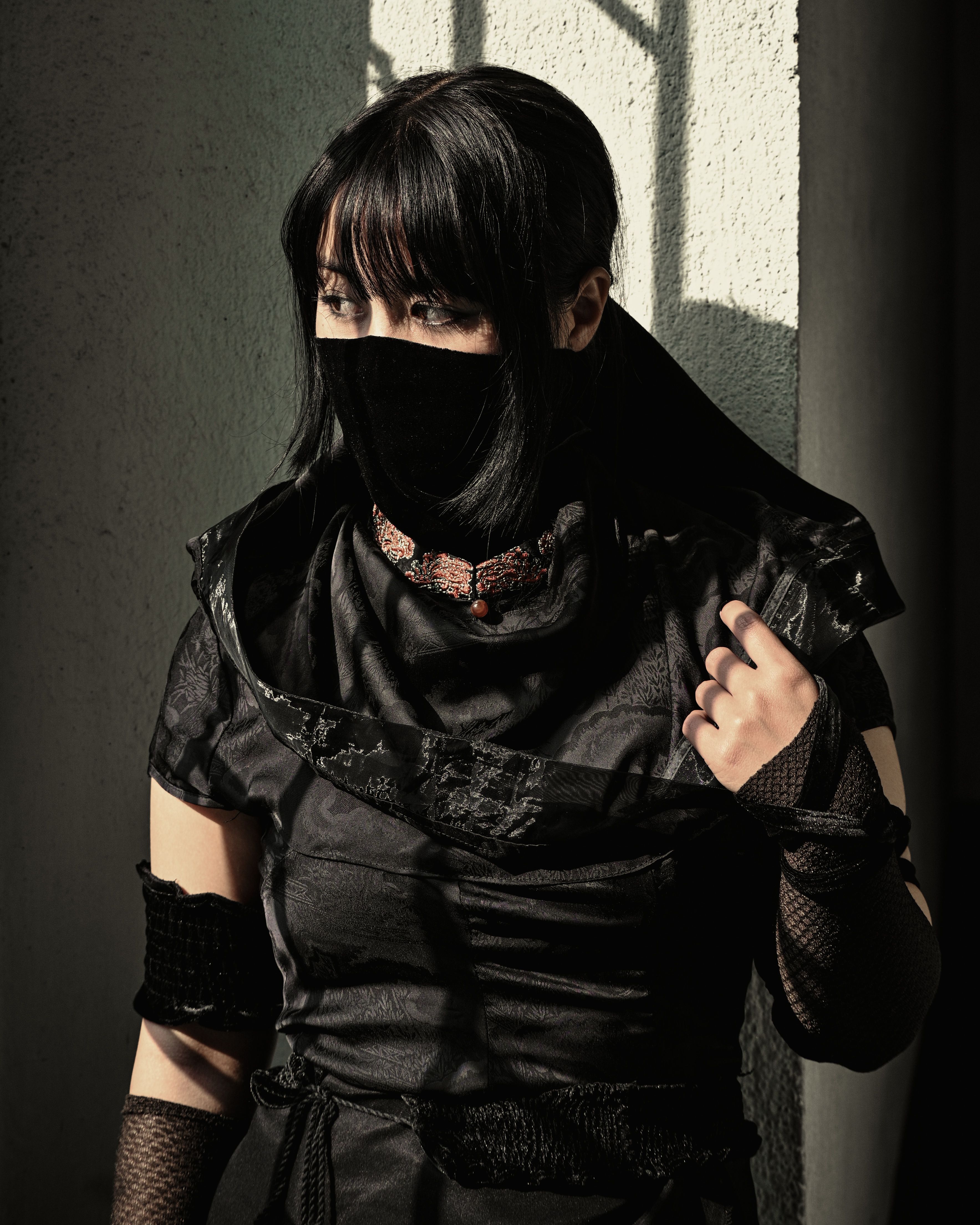 A woman in black attire stands in shadows, exuding mystery and intrigue.