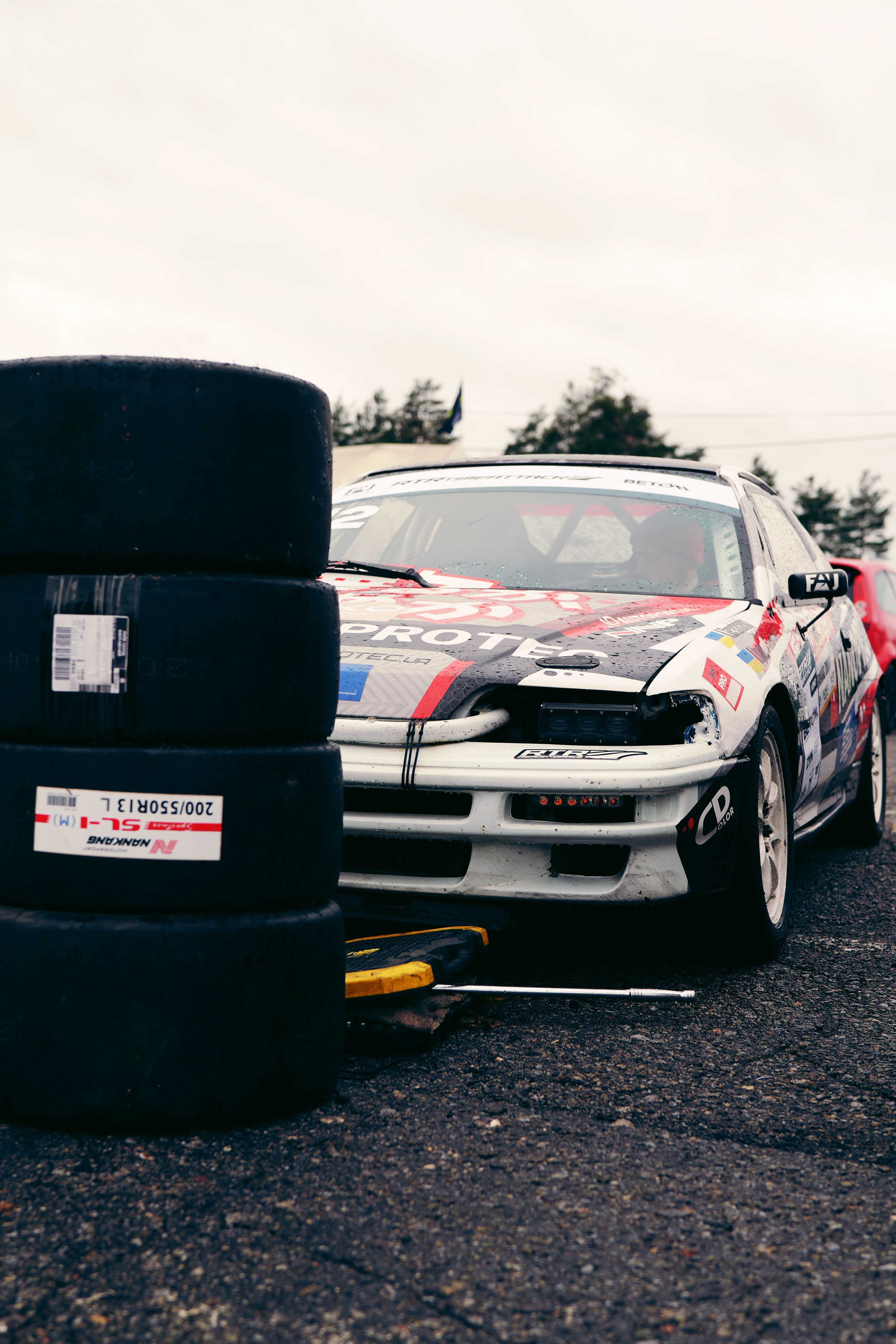 Vibrant sportscar with racing decals and stacked tires on a cloudy day at a racetrack in Ukraine.