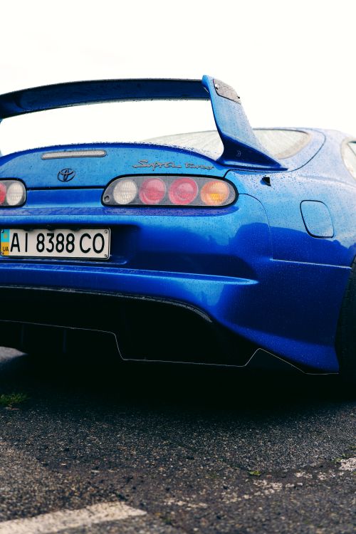 Free A striking blue sports car parked on a wet pavement in Ukraine, capturing the sleek design against a gray sky. Stock Photo