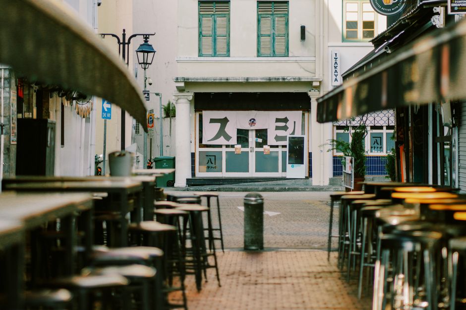 A quaint alley with empty tables and chairs leading to a shuttered building during daytime.