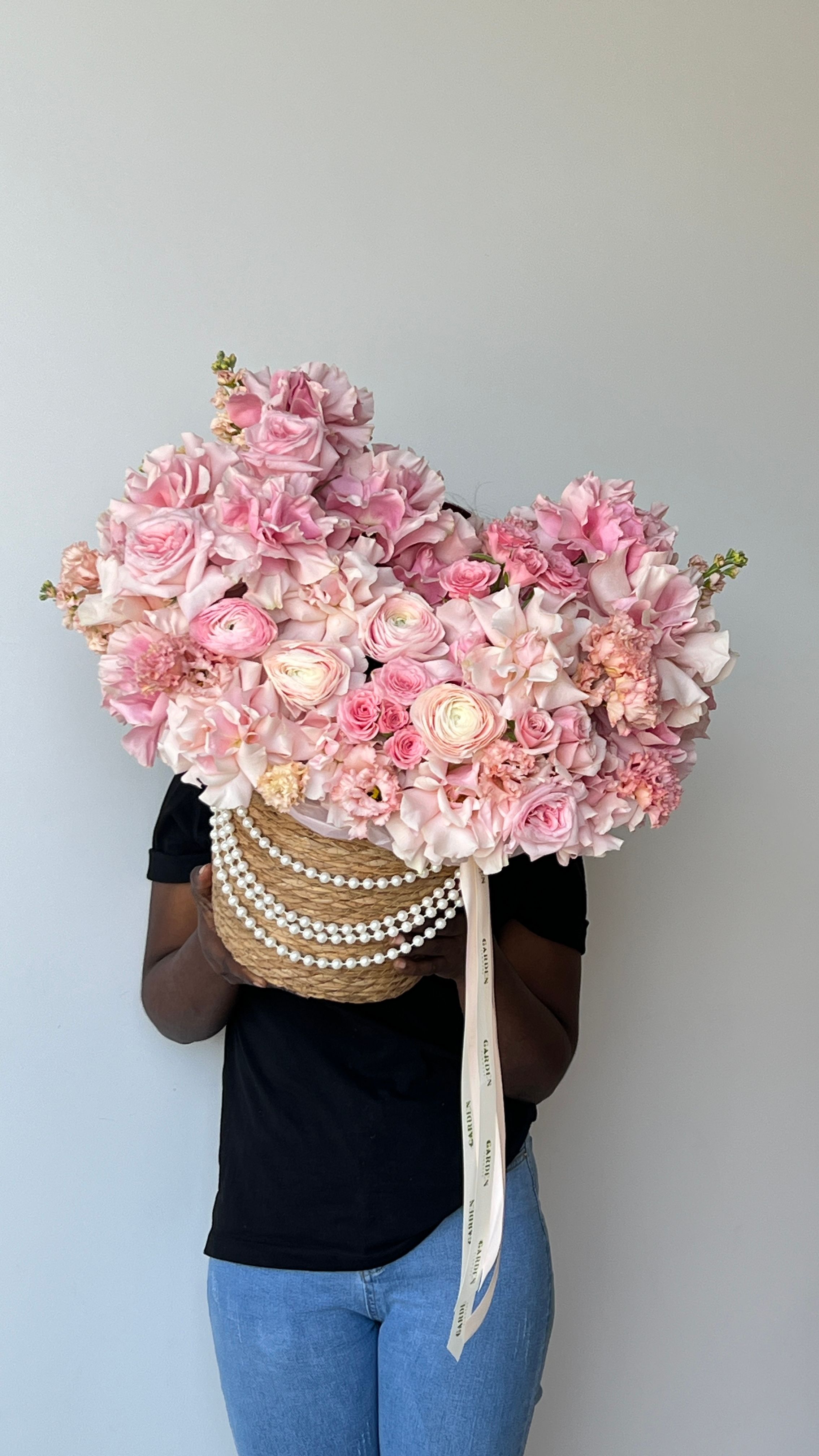 A striking bouquet of assorted pink flowers in a rattan basket held by a person against a clean background.