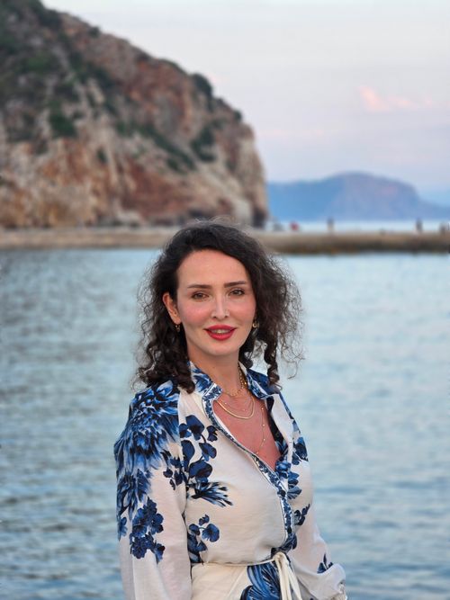 Free A cheerful woman stands by the sea with a scenic backdrop of Alanya, Turkey at sunset. Stock Photo