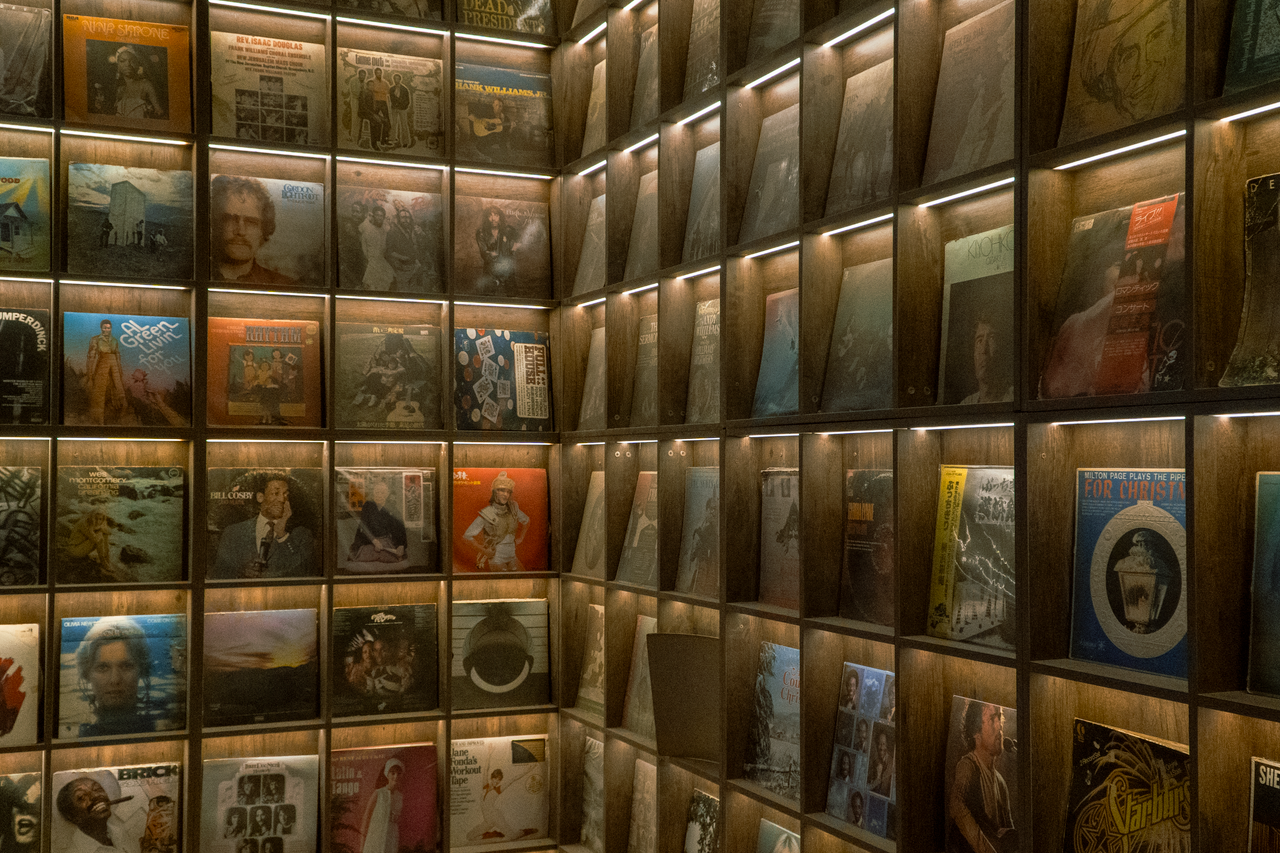 A wall of neatly arranged vintage vinyl records displayed on lit wooden shelves.