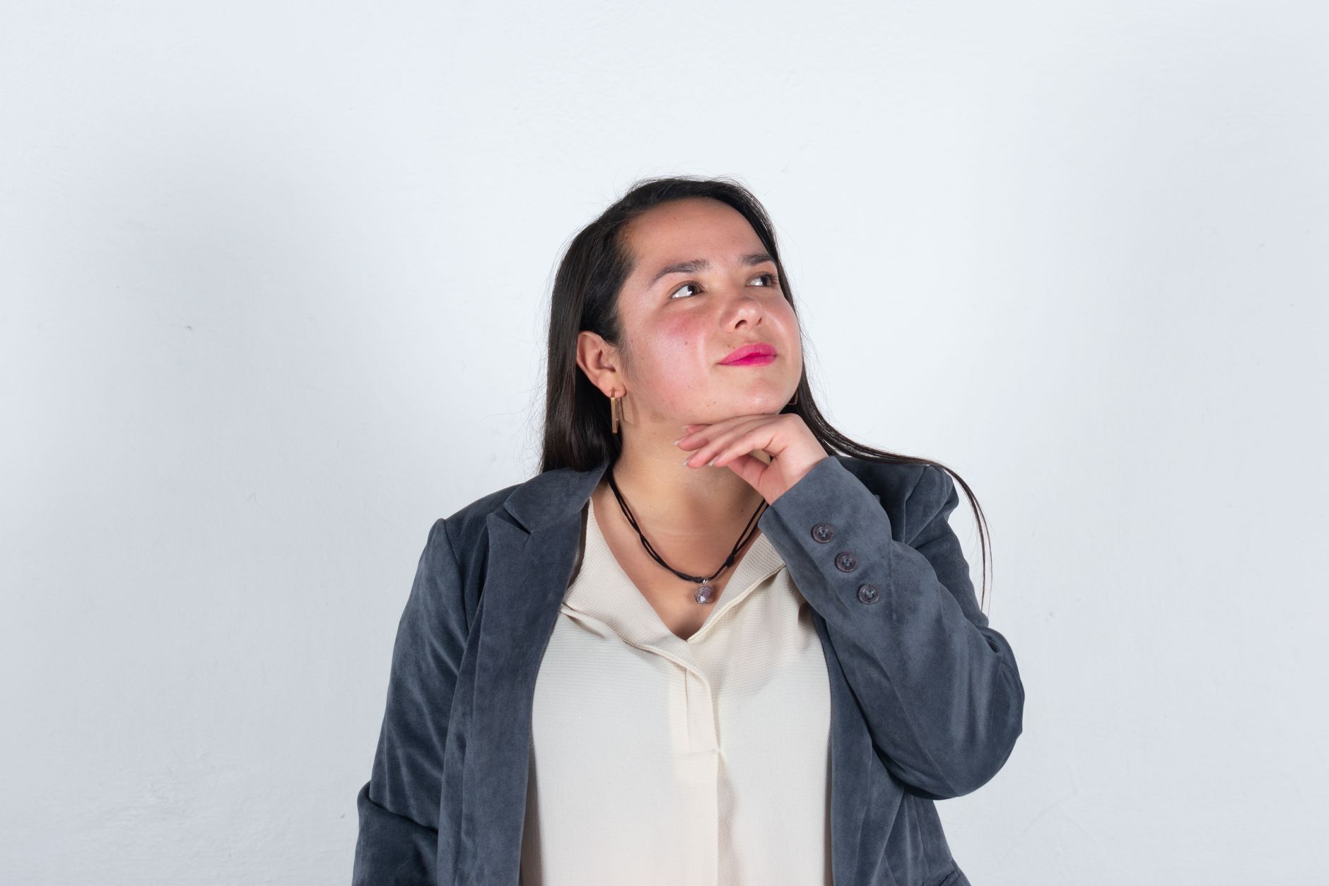 A thoughtful businesswoman in a grey suit poses against a white background, looking inspired.