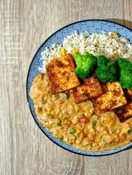 Delicious vegan curry tofu with rice and broccoli on a patterned plate.