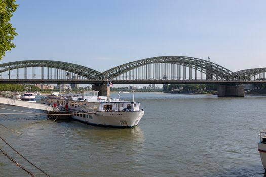 A scenic view of a boat docked at Hohenzollern Bridge in Cologne, Germany on a sunny day.