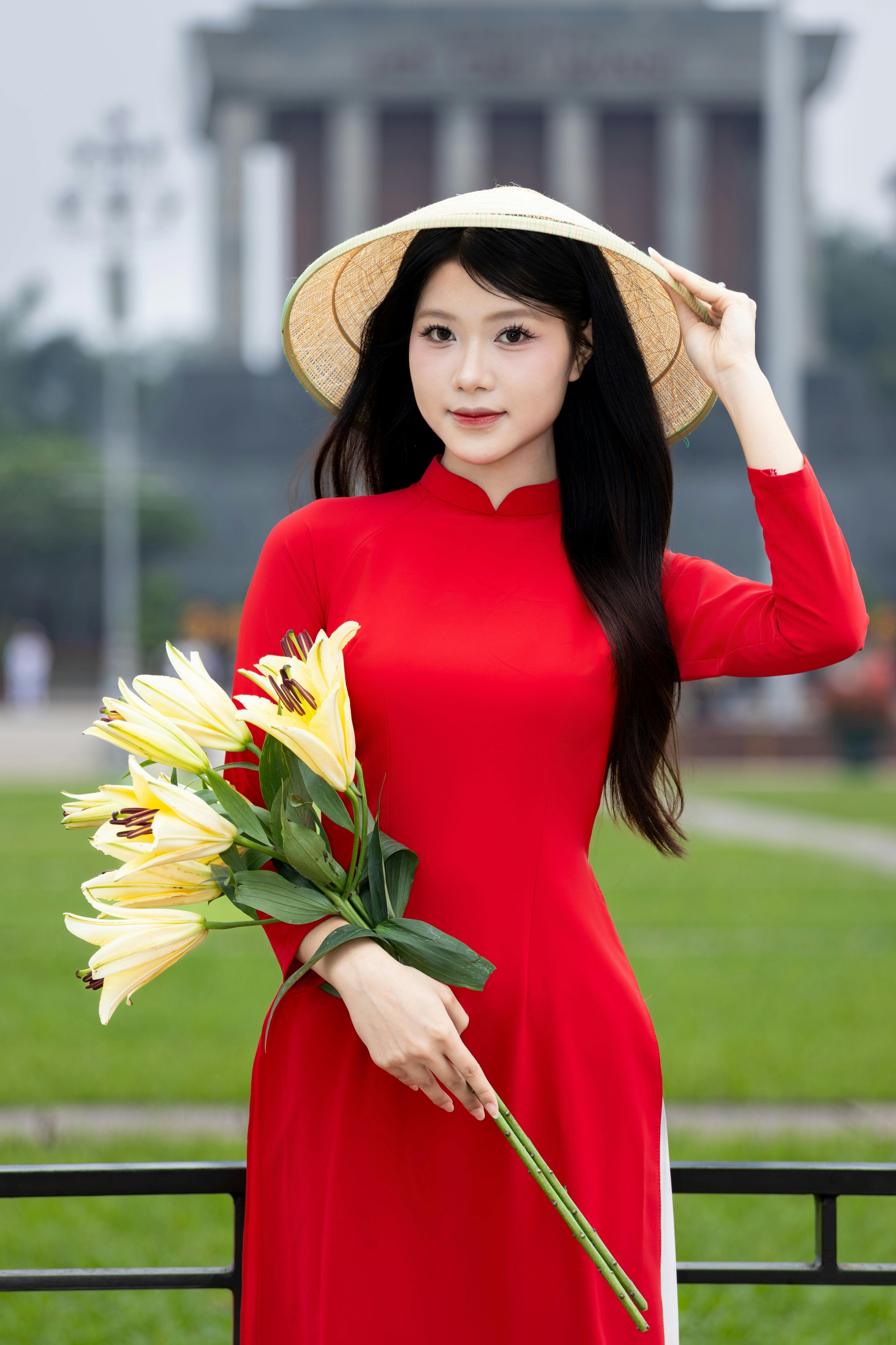Young woman in red Ao Dai holding lilies in Hà Nội's park, embodying Vietnamese culture.