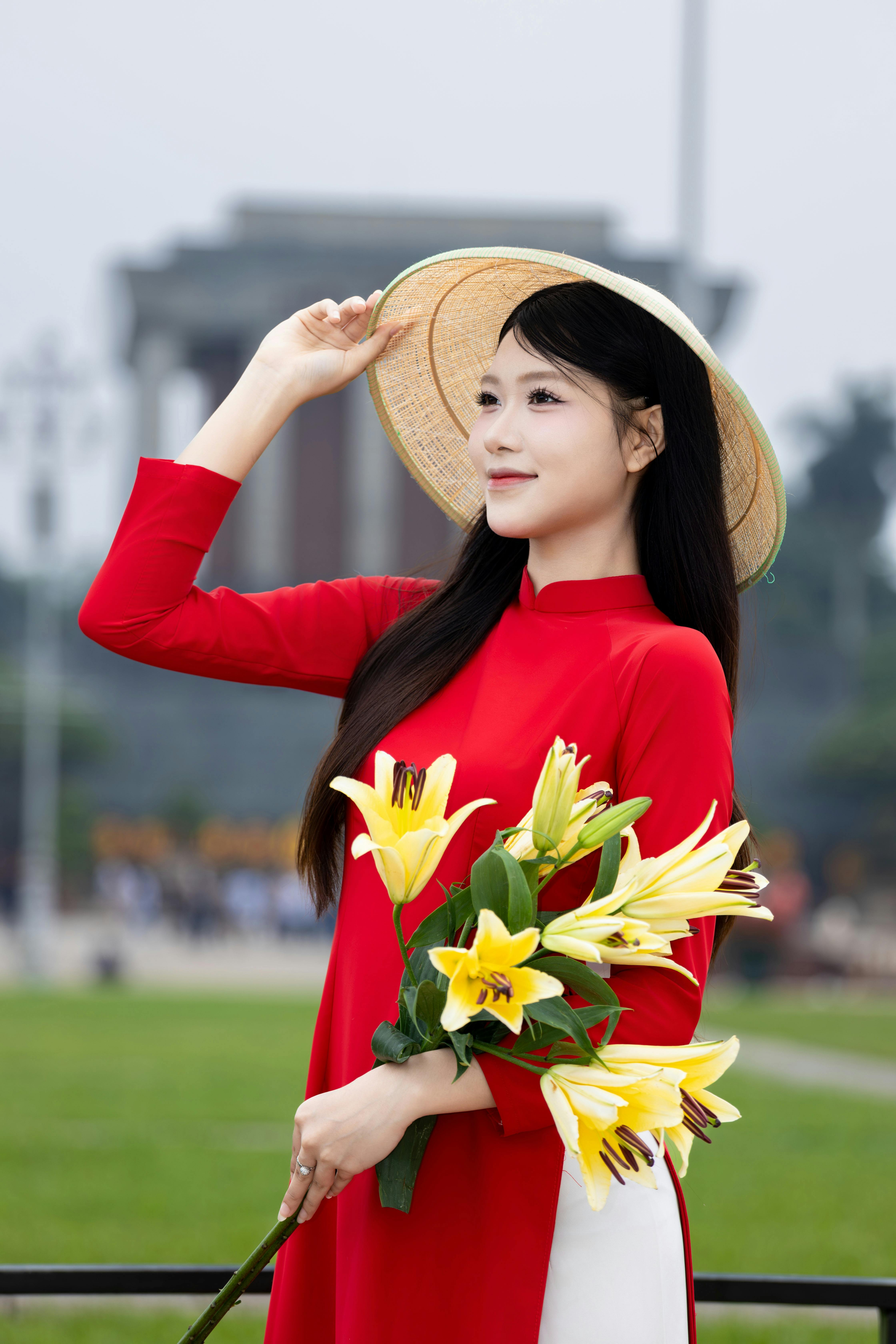 Beautiful Asian woman in red ao dai holding lilies outdoors in Hà Nội.