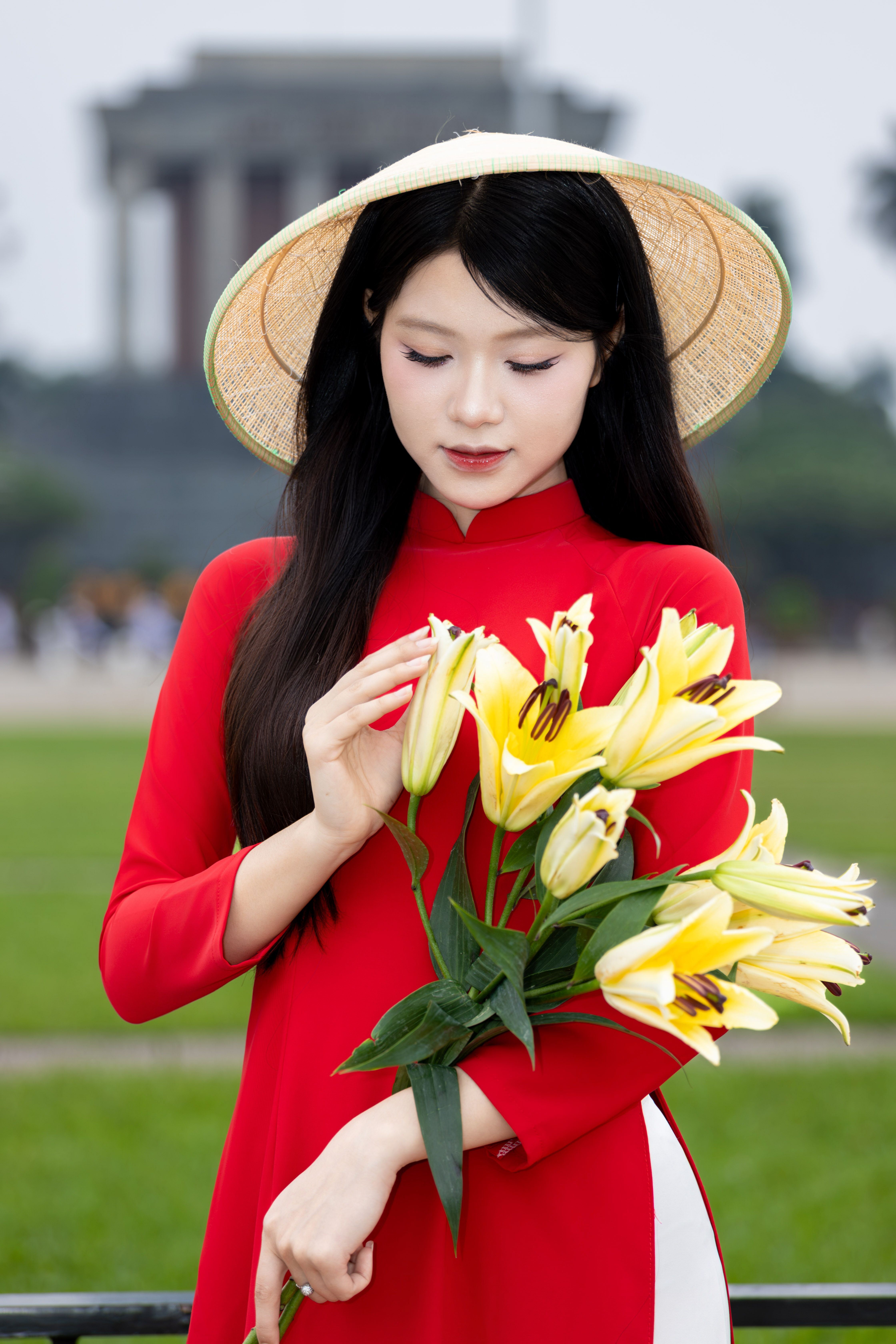 Woman in red ao dai holding yellow lilies in Hanoi, Vietnam.