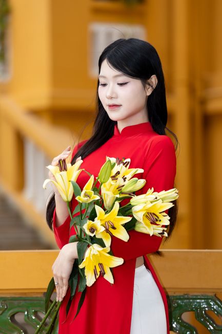 Young woman in traditional Vietnamese Ao Dai holding a bouquet of yellow lilies outdoors.