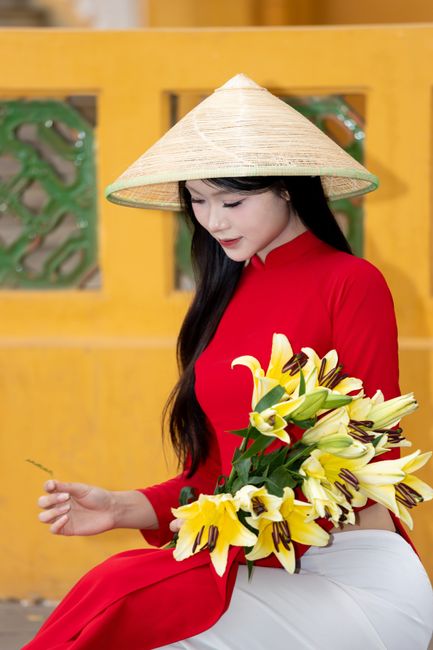 A Vietnamese woman in a traditional Ao Dai holds lilies, symbolizing elegance in Hanoi.