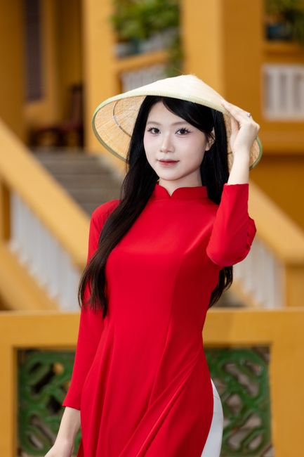 Elegant Vietnamese woman in traditional red ao dai and nón lá hat, Hà Nội street view.
