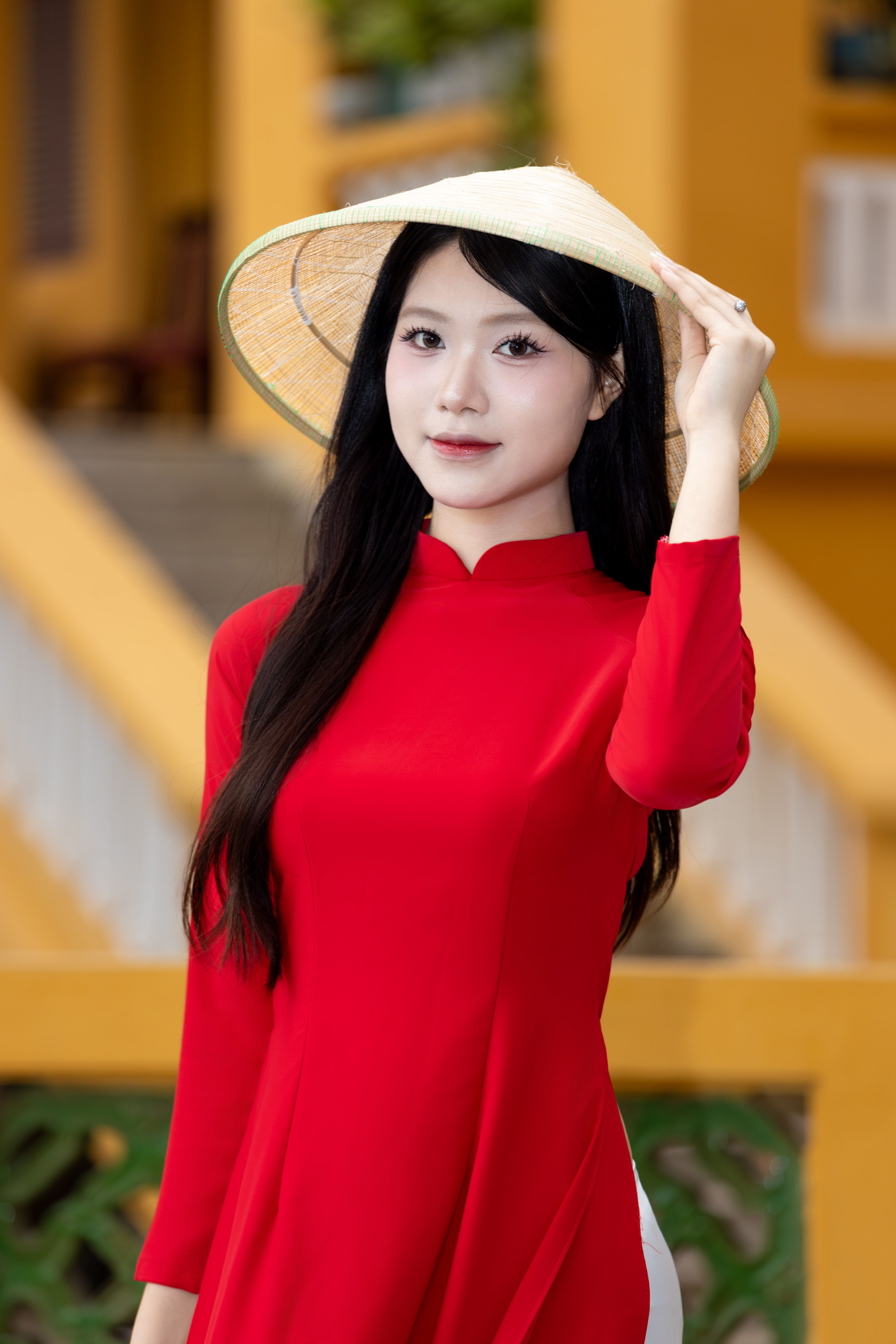 A woman wearing a red áo dài and a conical hat in Hanoi, Vietnam.
