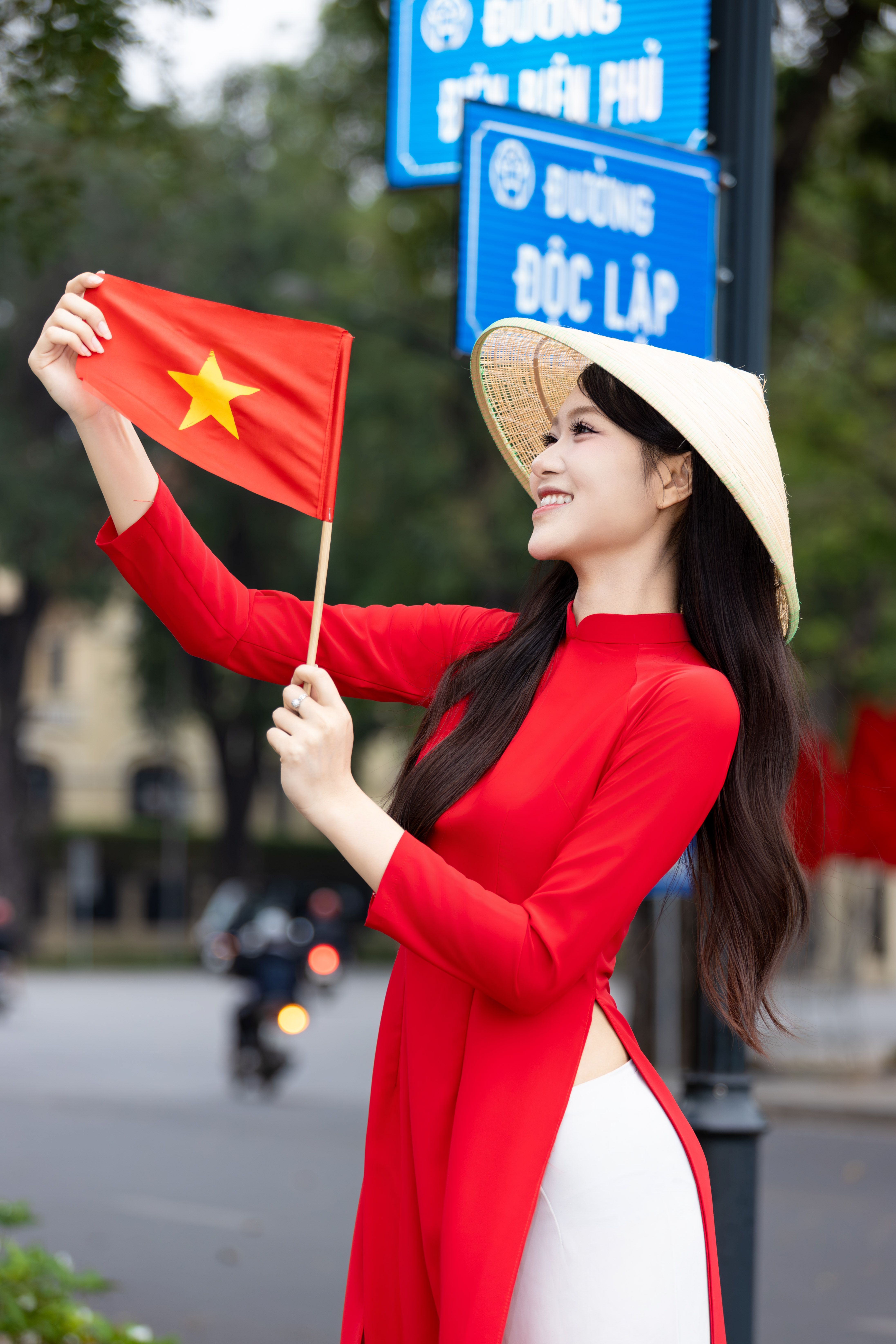 Woman in traditional dress holding Vietnamese flag on Hanoi street.