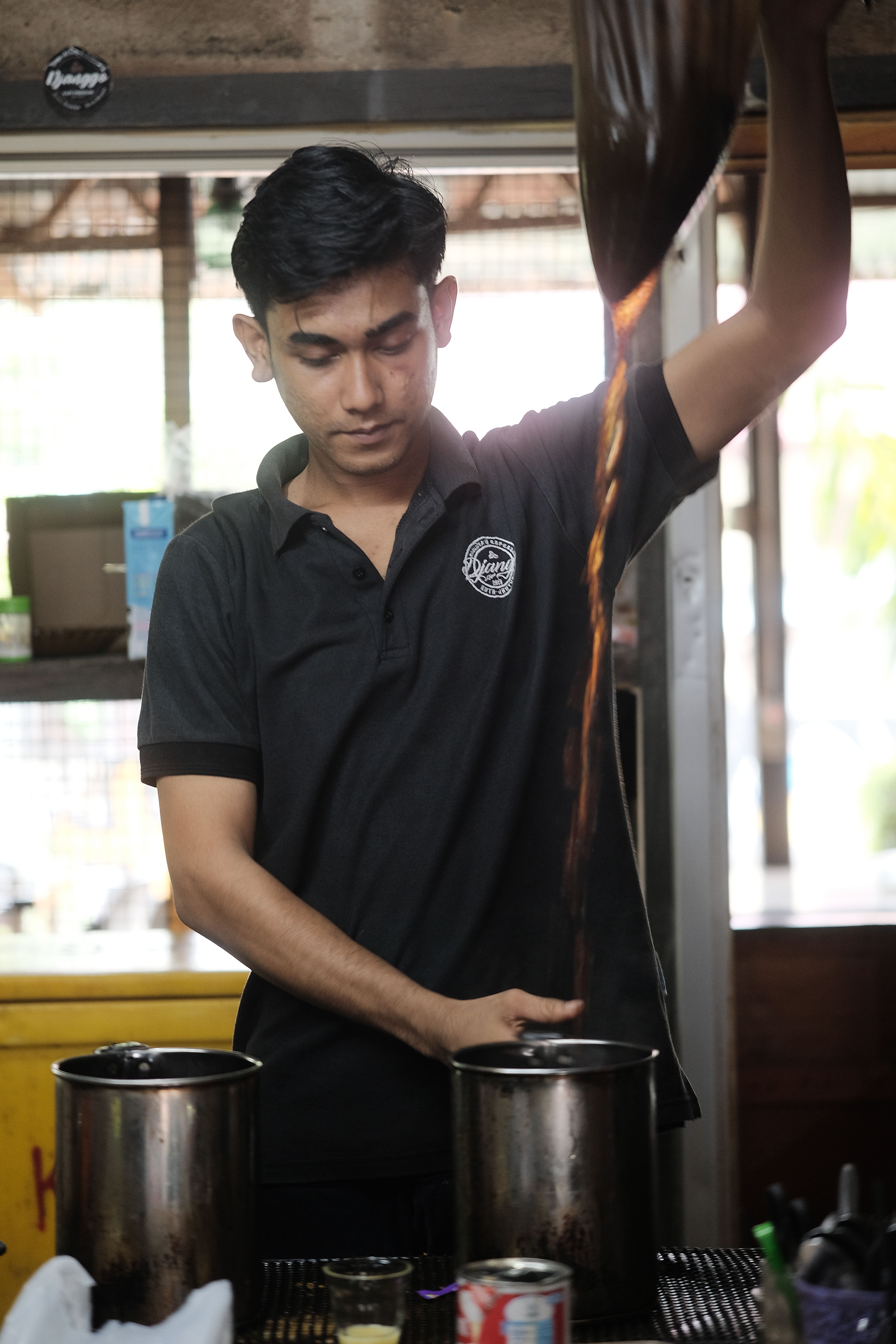 Barista in Indonesia demonstrates traditional coffee pouring technique with precision and skill.