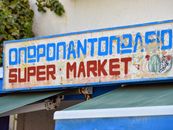 Vintage supermarket sign featuring Greek text and vibrant illustrations captured in natural light.
