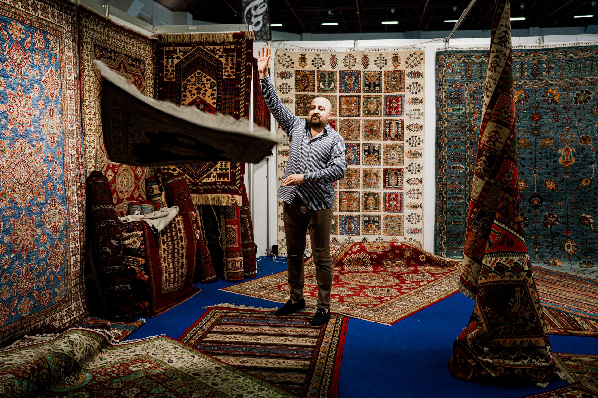 Trade show booth with a vendor displaying patterned rugs on a show floor