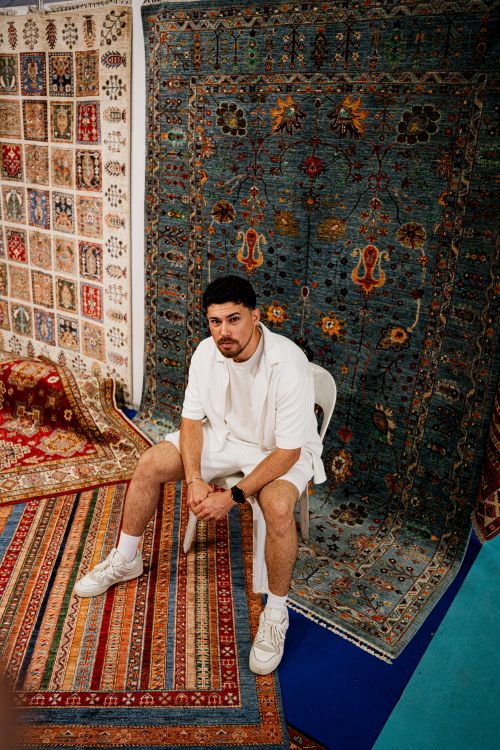 Free Young man seated in a colorful rug store, showcasing diverse designs and patterns. Stock Photo