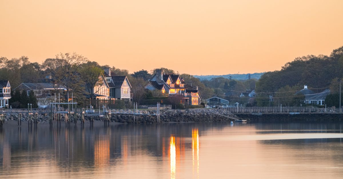 Charming coastal homes reflected on calm waters during sunset, evoking tranquility.