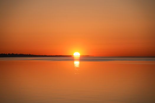 A tranquil sunrise over a calm ocean, casting a warm golden reflection on the water.