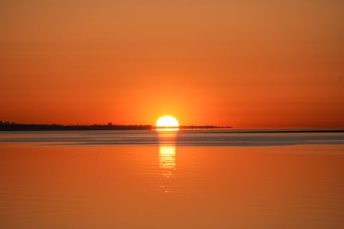 Free A tranquil sunset scene with vibrant orange hues reflecting on the calm ocean waters. Stock Photo
