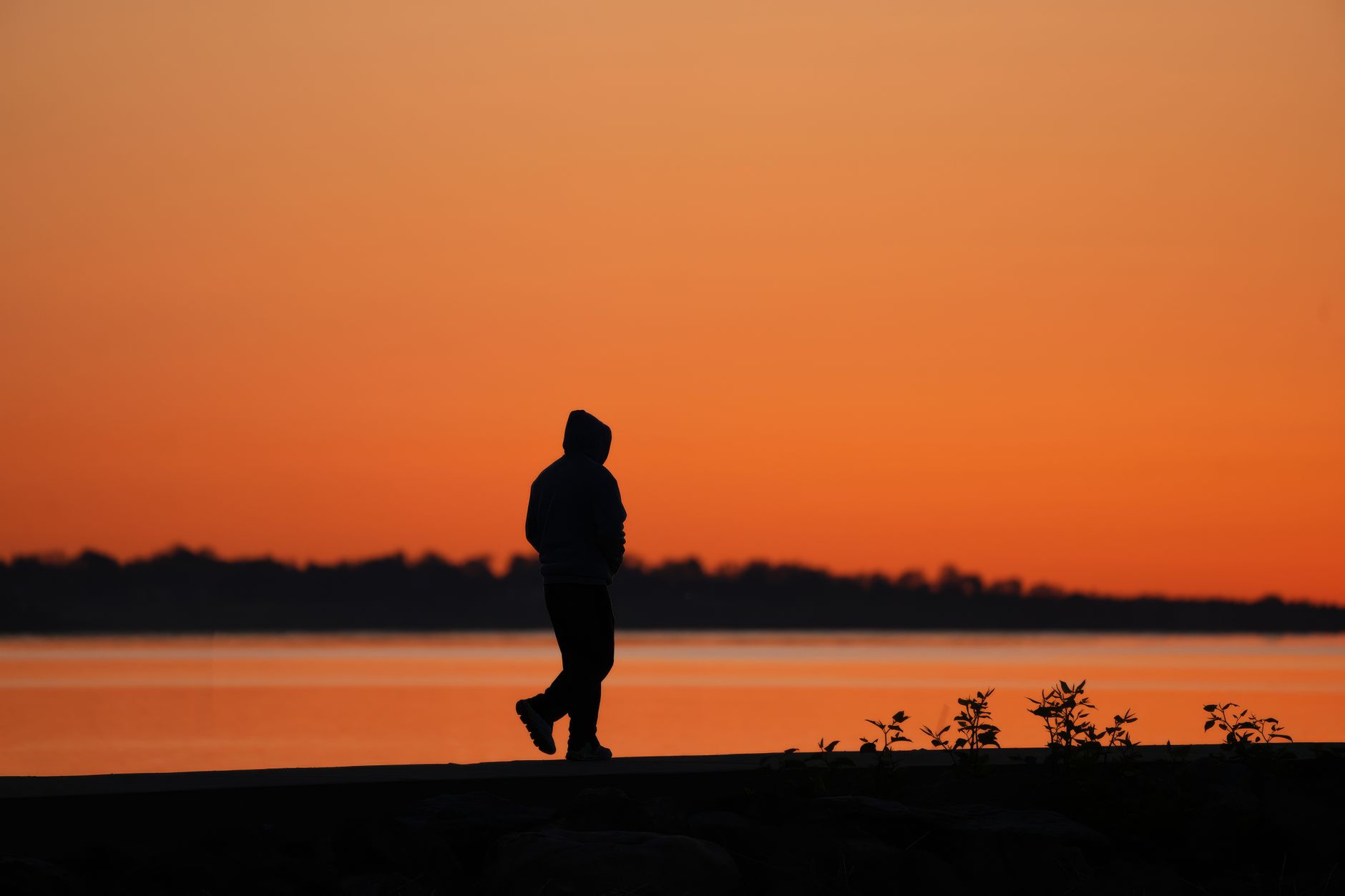 A person in silhouette walks along a lakeside path against a vibrant sunset backdrop.