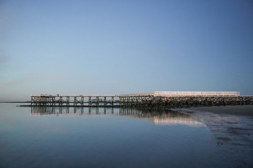 Free Calm ocean view with a wooden pier reflecting in the serene water during dusk. Stock Photo