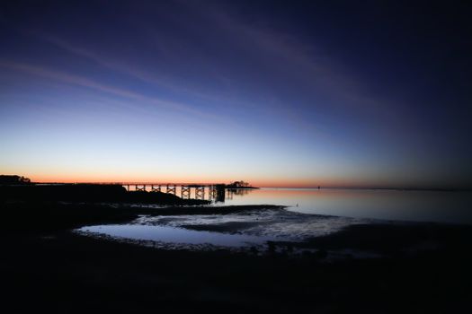Peaceful twilight view of a coastal pier with calm waters and vivid sky colors.