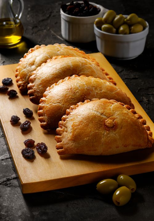 Free Tasty Peruvian empanadas on wooden board with olives and raisins, perfect for gastronomy enthusiasts. Stock Photo