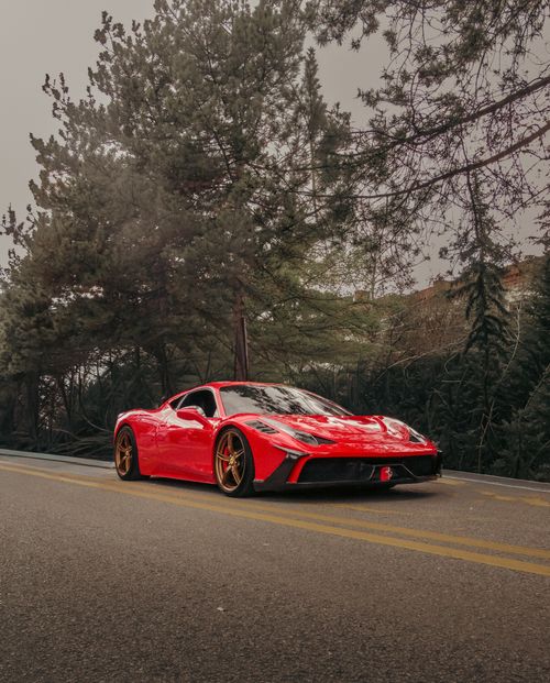 Free Elegant red sports car parked on a scenic road framed by lush trees, captured in Ankara, Türkiye. Stock Photo
