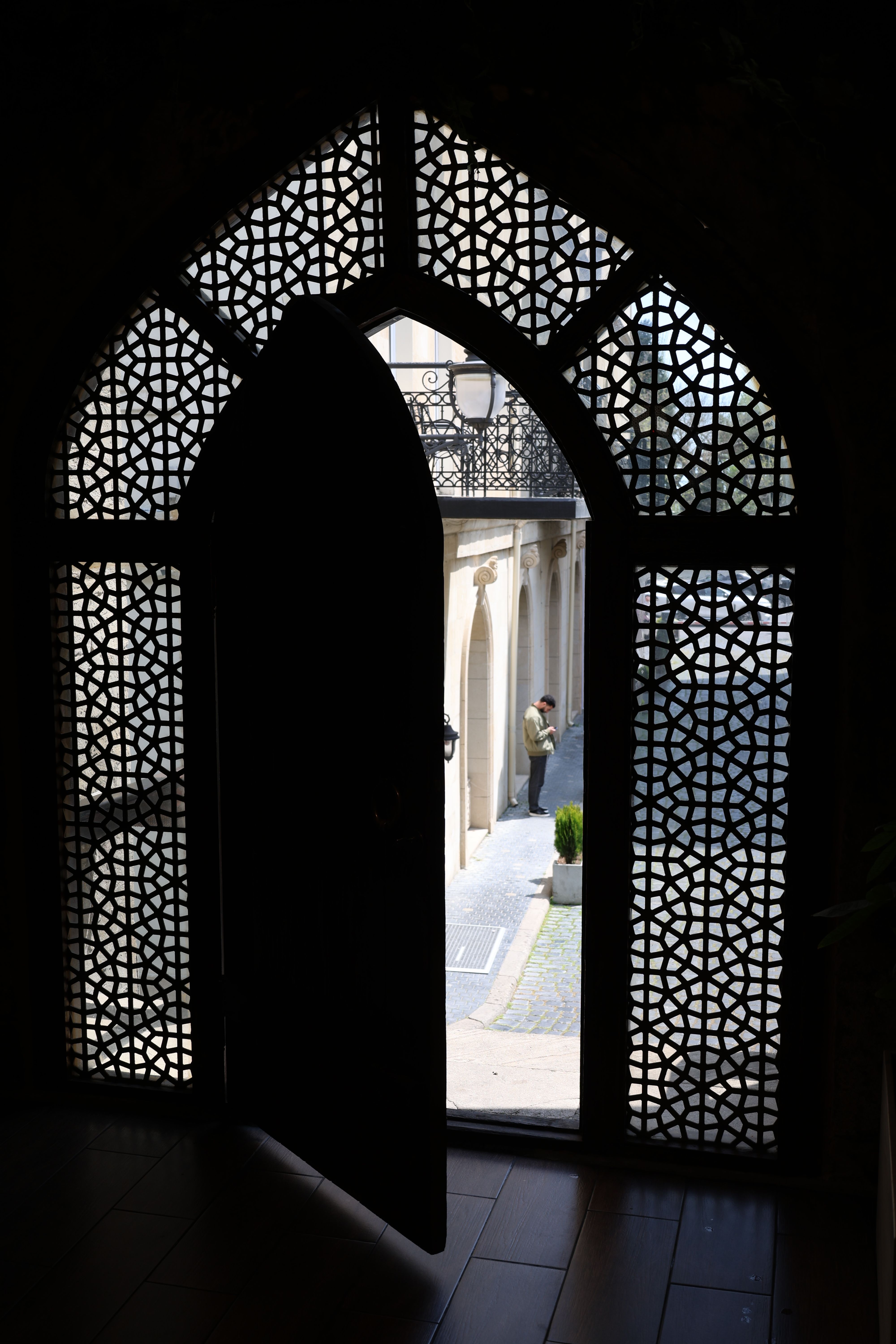 Free Sunlight streams through an ornate archway, revealing a person on a sunlit urban street. Stock Photo