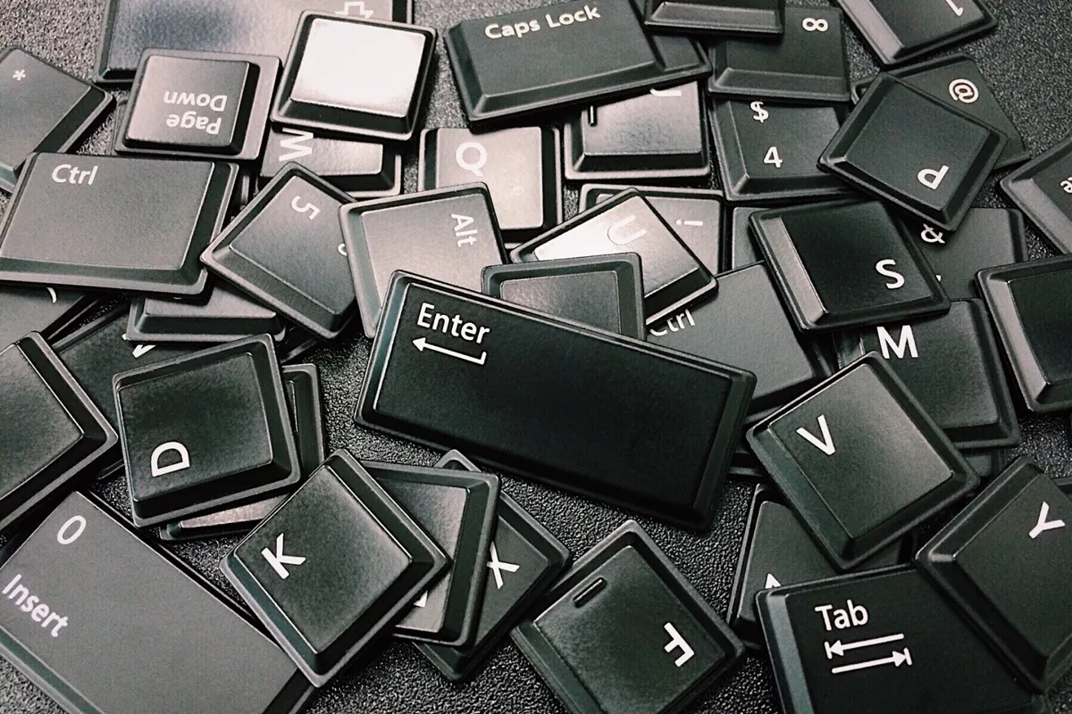 Close-up of scattered black computer keyboard keys on a surface, showcasing various letters and symbols.