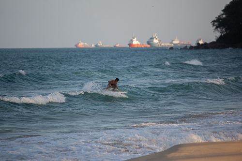 Free A dynamic shot of a surfer skillfully riding the ocean waves with multiple ships visible in the distance. Stock Photo