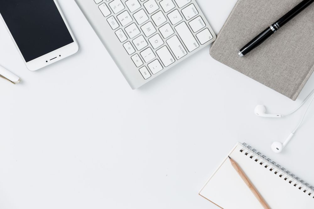 A phone, keyboard and notebook on a clean desk