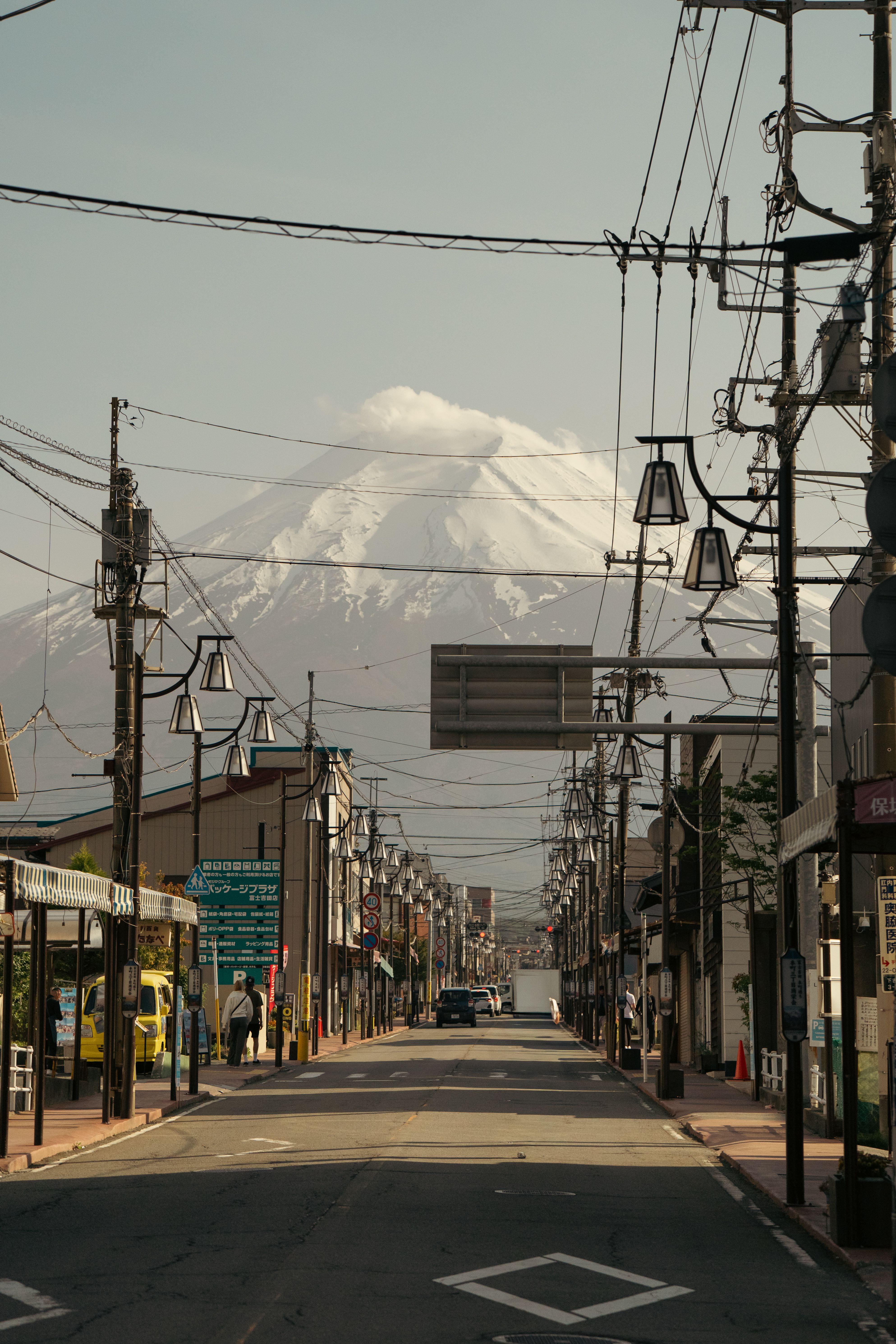 Mount Fuji rises over a quaint Japanese street, framed by power lines and clear skies.