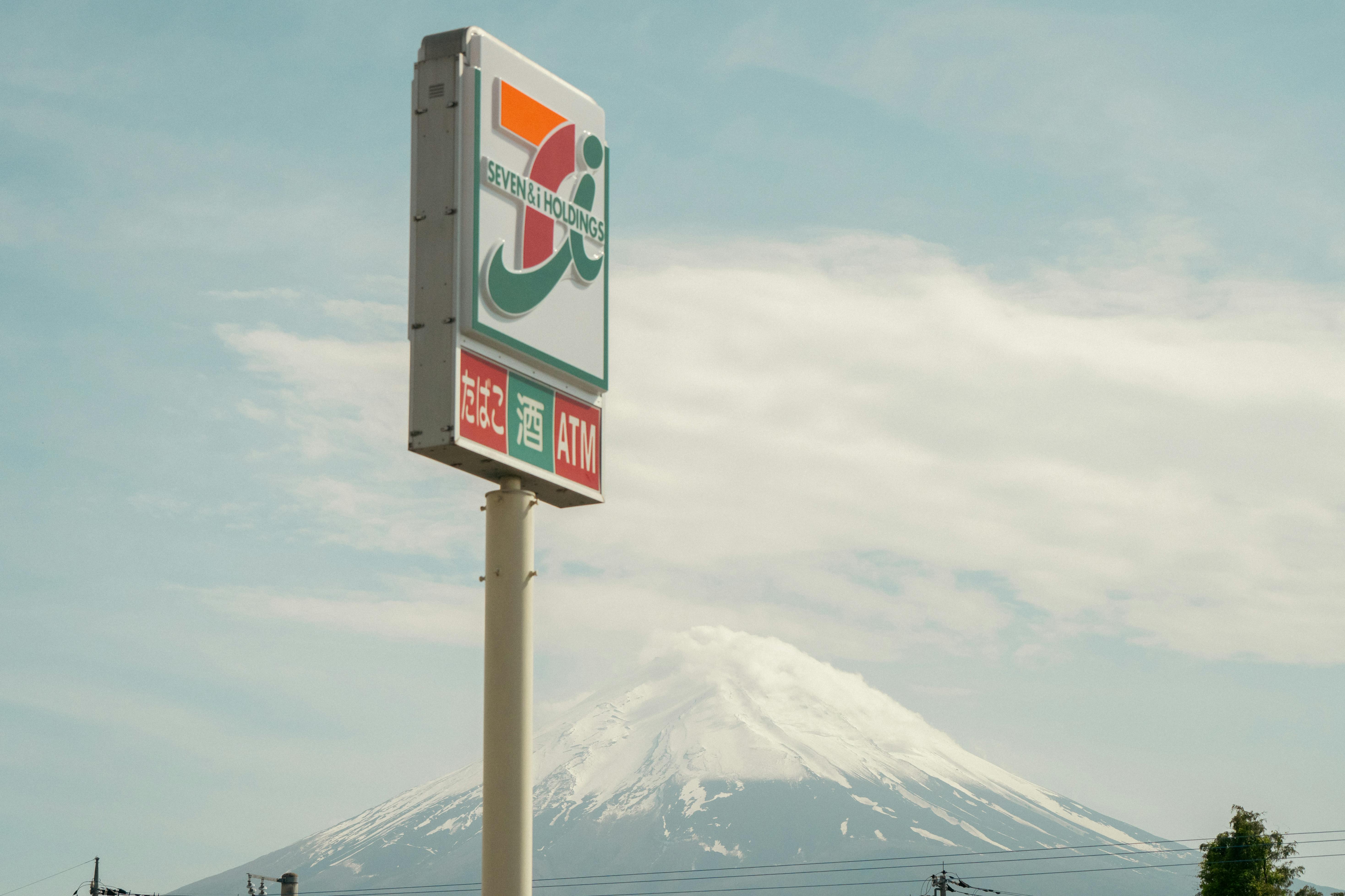 A sign for a convenience store with Mount Fuji in the background under a clear sky.