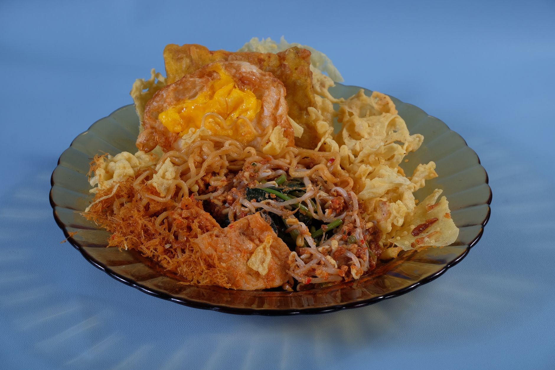 Savor a delicious mixed plate featuring Indonesian street food with noodles, egg, and crispy elements.