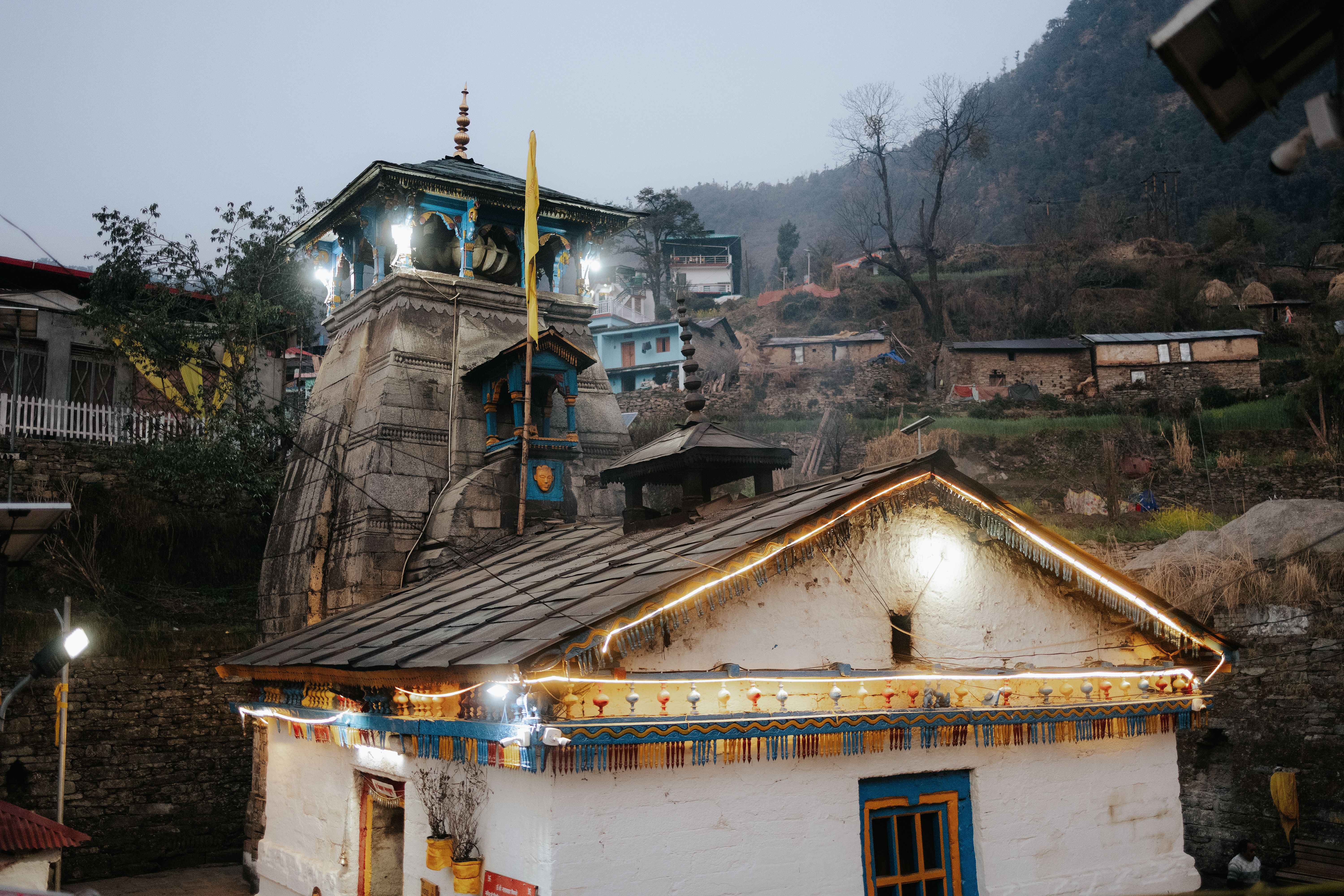 Serene view of an illuminated temple amidst traditional Indian village architecture at twilight.