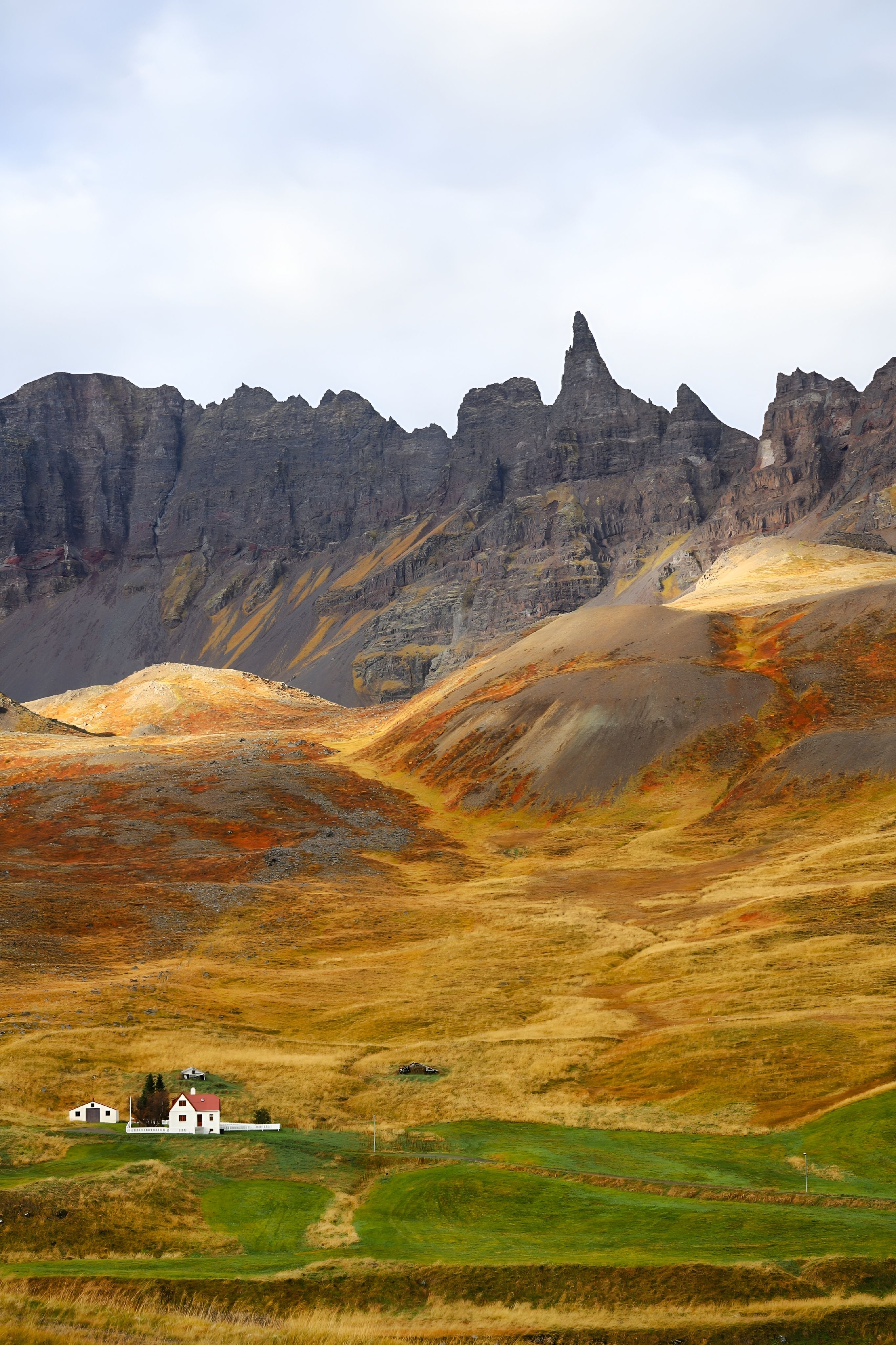 A solitary house amidst vibrant autumn mountains with dramatic peaks.