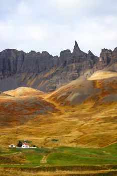 A solitary house amidst vibrant autumn mountains with dramatic peaks.