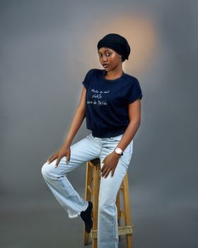 Young woman in casual attire posing confidently on a wooden stool.