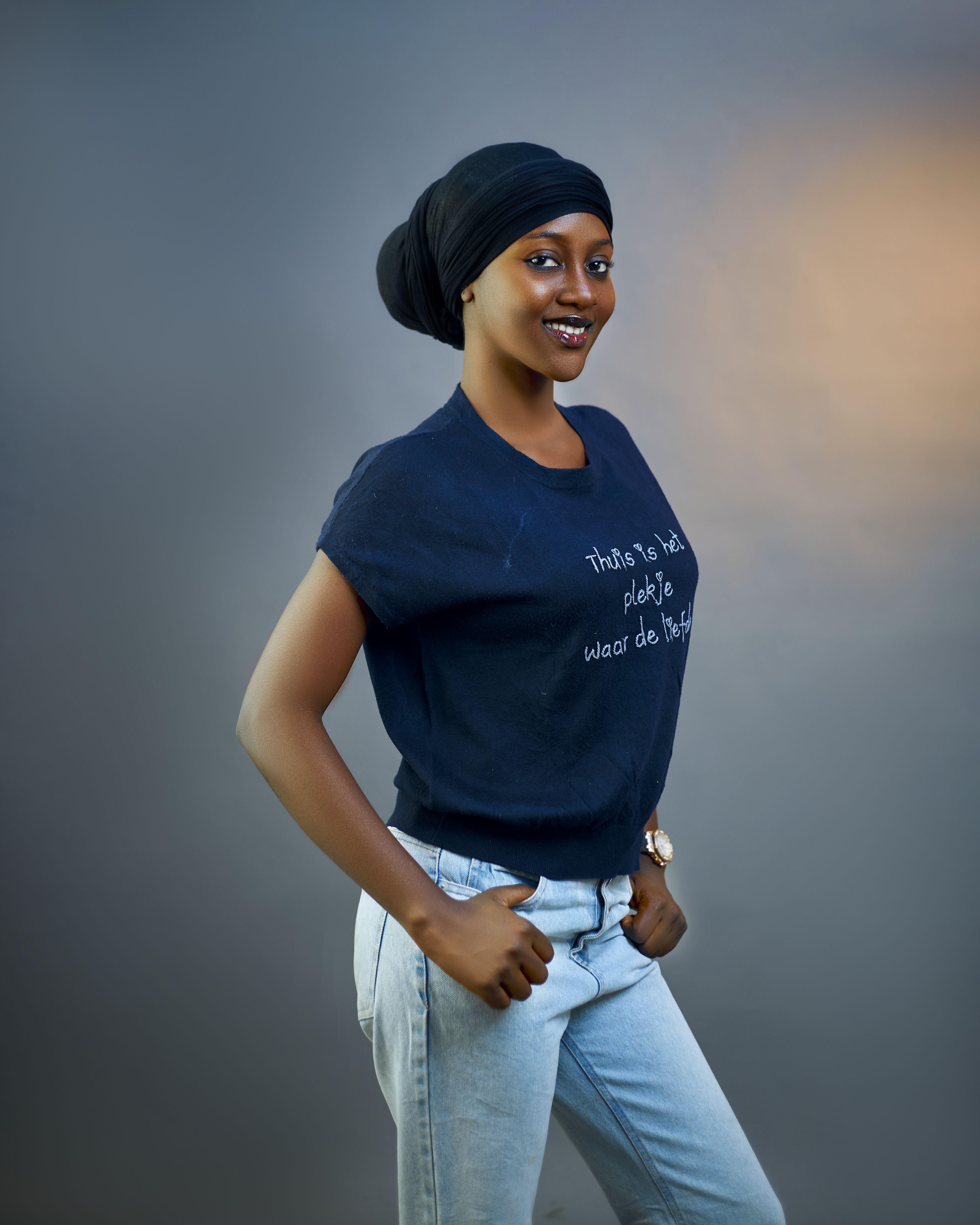 A young woman in casual attire smiling confidently in a studio portrait shot.