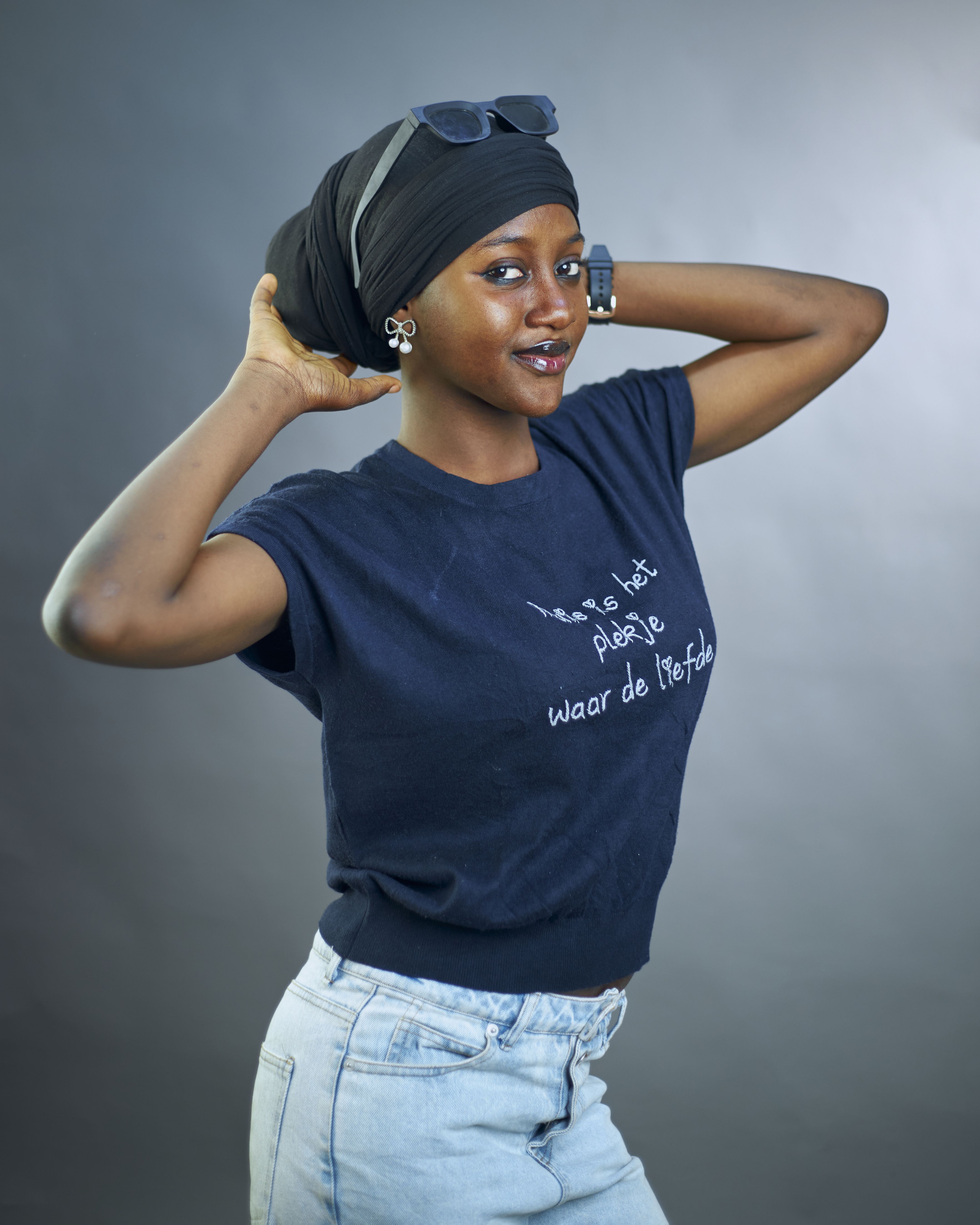 Young woman posing confidently in a studio with a stylish outfit and accessories.