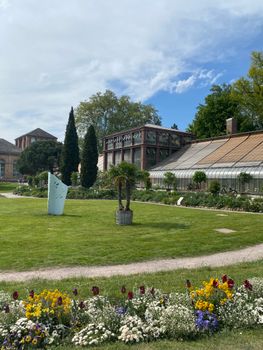 A scenic view of Karlsruhe's botanical garden with vibrant flowers and historic buildings under a clear sky.